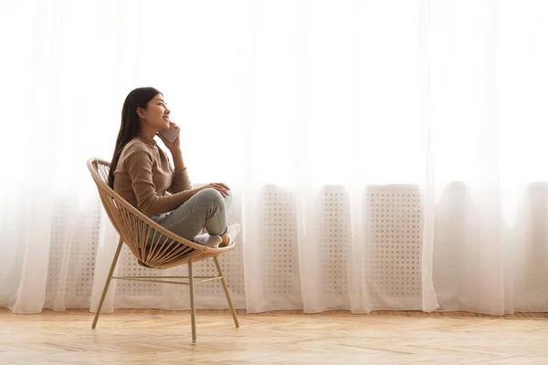 Desfrutando de conforto em casa. Menina falando no telefone na cadeira aconchegante — Fotografia de Stock