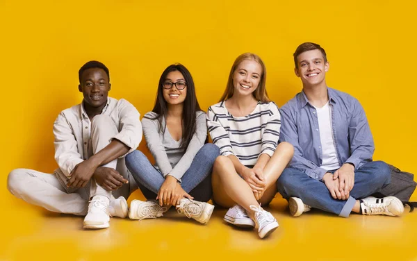 Happy students posing over yellow studio background — Stockfoto
