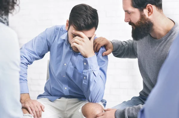 Concerned patients comforting upset man at group therapy session in rehab