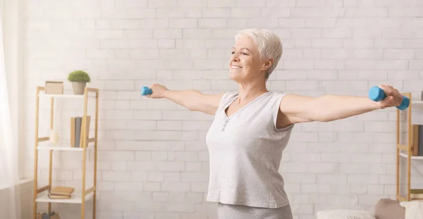 Активная старшая женщина делает упражнения с гантелями дома — стоковое фото