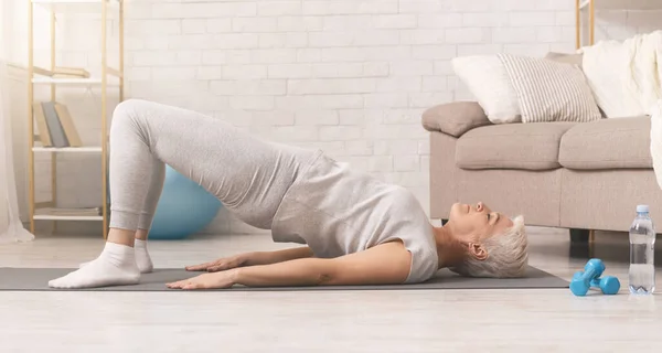 Активная пожилая женщина делает упражнения для спины на полу дома — стоковое фото