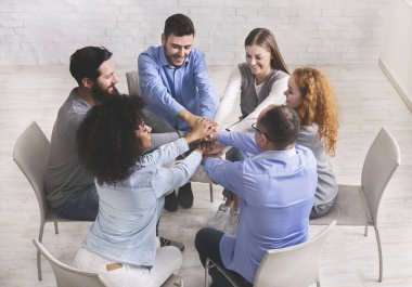 Çemberde oturan ve elleri üst üste yığan mutlu insanlar başarılı rehabilitasyonu kutluyorlar.