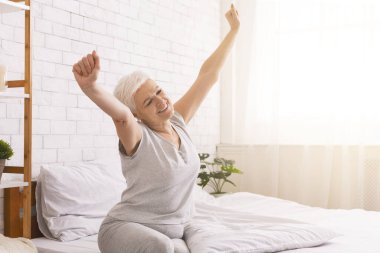 İyi uyuyan yaşlı kadın sabahları yatakta geriniyor.