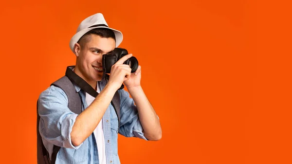 Active happy traveler taking photos, using camera over orange background