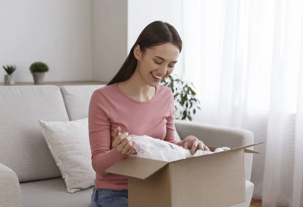 Overblij jong meisje zitten op de bank en unboxing geleverd pakket — Stockfoto