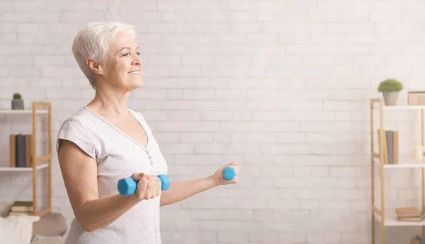 Deportiva mujer mayor haciendo ejercicio con mancuernas en casa — Foto de Stock