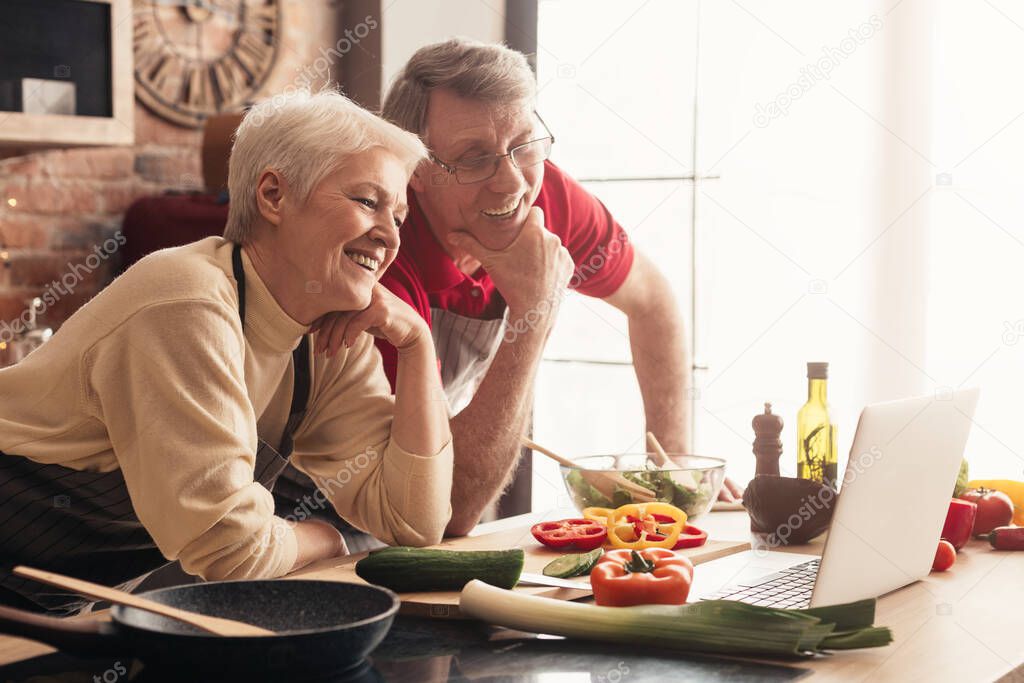 Cheerful Senior Couple Using Laptop In Kitchen, Watching Culinary Recipies Together