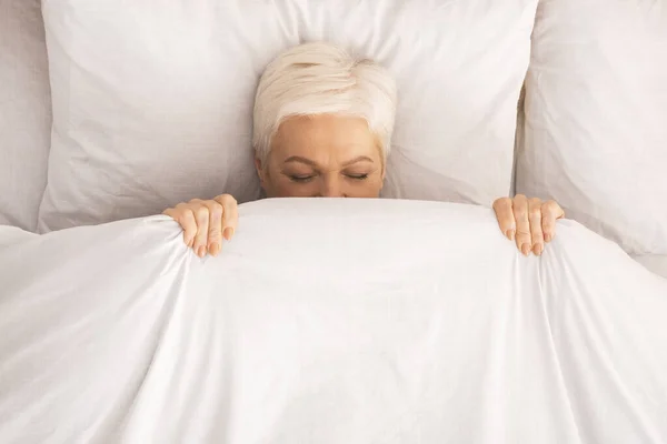 Señora jubilada acostada en la cama y jugando al escondite — Foto de Stock