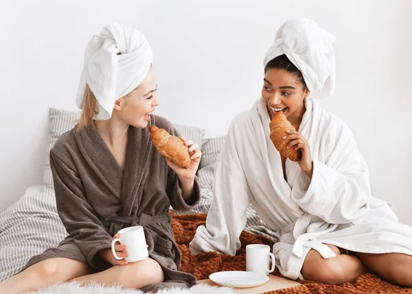 Namoradas multiétnicas em roupões de banho tomando café da manhã na cama — Fotografia de Stock