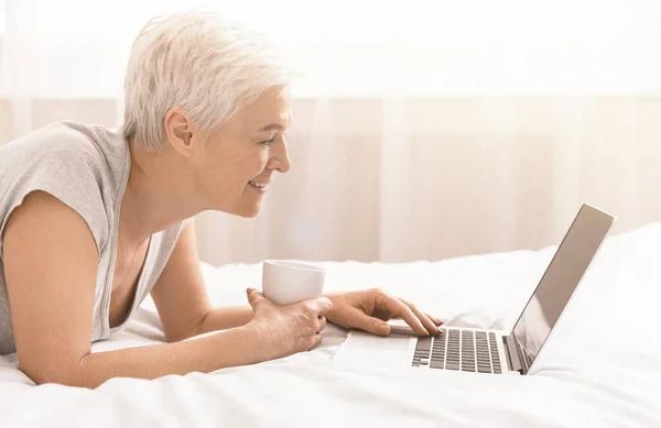 Senior lady browsing on laptop and enjoying morning coffee — Stock Photo, Image