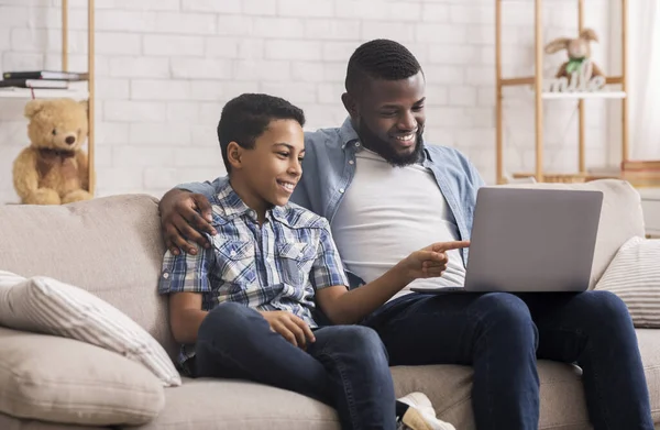 Ayah muda dan anak remaja menggunakan laptop di rumah bersama-sama — Stok Foto