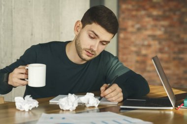 Çok çalışan çalışanın elinde kahve fincanı var, neredeyse işyerinde uyuyor.