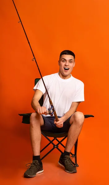 Nadšený mladý muž sedí na židli a rybaření — Stock fotografie
