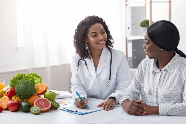 Amical afro dame nutritionniste faire l'anamnèse du patient à la clinique — Photo