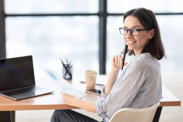 Leende ung kvinnlig arbetare sitter med bärbar dator — Stockfoto