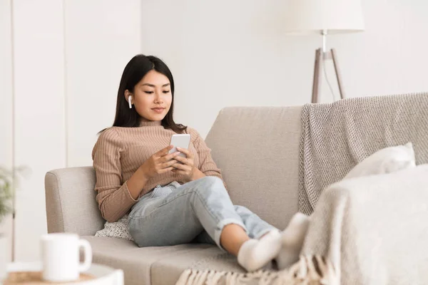 Relajada chica acostada en el sofá y el uso de teléfono —  Fotos de Stock