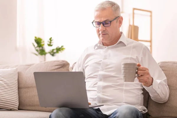 Ηλικιωμένος άνθρωπος χρησιμοποιώντας φορητό υπολογιστή και έχοντας τσάι — Φωτογραφία Αρχείου