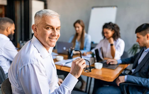 Mature Businessman Smiling Sitting At Corporate Meeting In Office