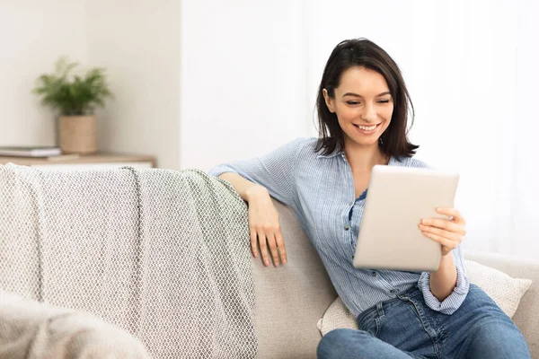 Mujer joven usando tableta digital sentada en el sofá — Foto de Stock