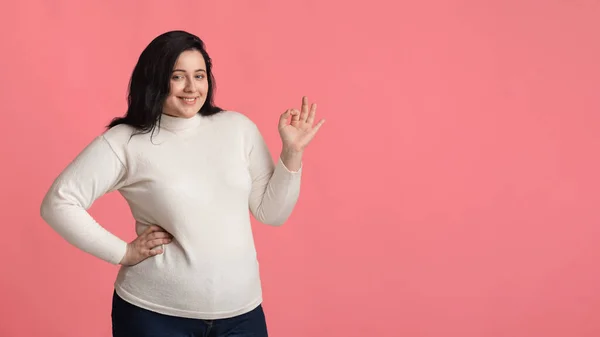 Positive mollige Frau gestikuliert Okay-Zeichen und posiert vor rosa Hintergrund — Stockfoto