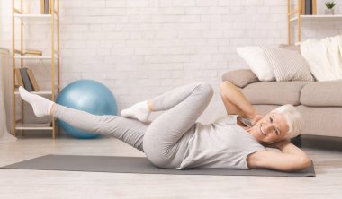 Sporty senior woman doing abs exercise on floor at home