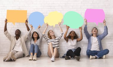 Group of teenagers sitting on floor, holding speech bubbles above