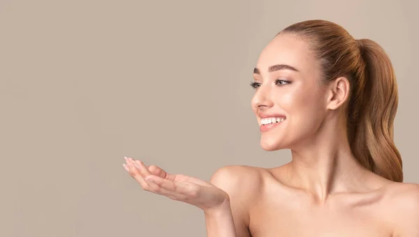 Woman Posing Holding Invisible Object On Hand Over Beige Background — Stock Fotó