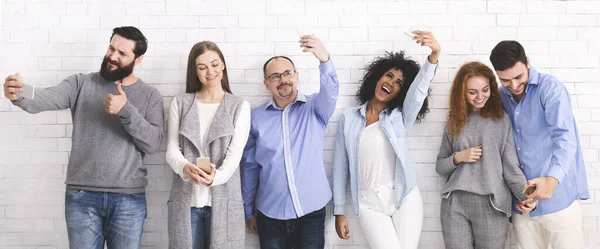 Group of friends taking selfie with smartphones, posing over white wall — Stock Photo, Image