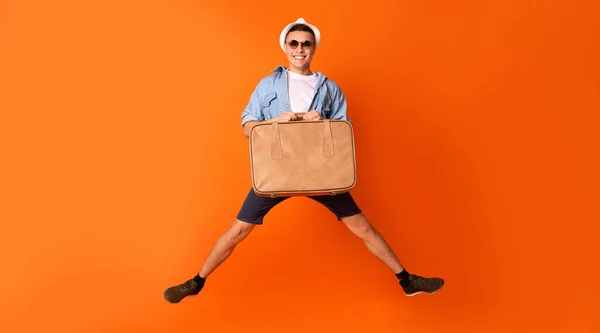 Счастливый турист прыгает с чемоданом на оранжевом фоне — стоковое фото