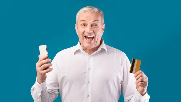 Homem maduro feliz segurando cartão de crédito e celular — Fotografia de Stock