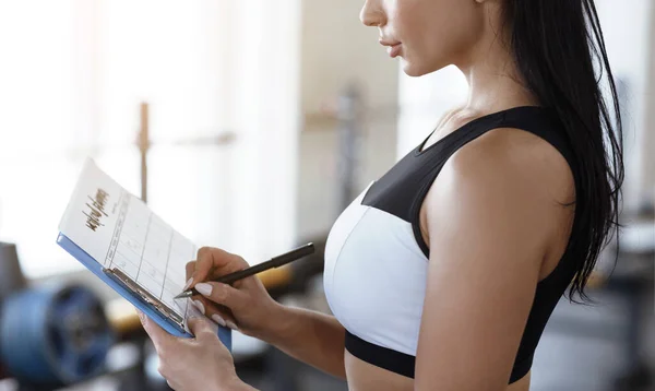 Workout planning. Young woman keeping track of her trainings in gym, closeup — Stockfoto