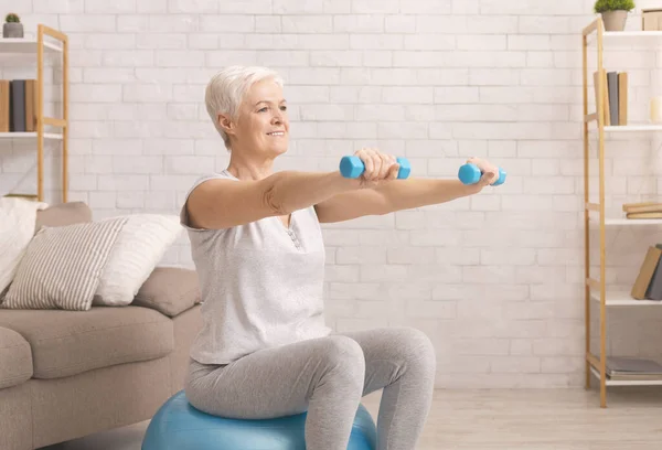 Senior mulher em sportswear exercício com halteres em casa — Fotografia de Stock