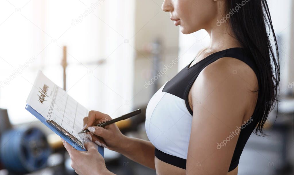 Workout planning. Young woman keeping track of her trainings in gym, closeup
