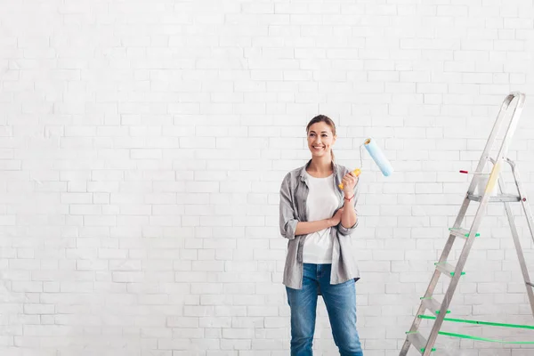 Thoughtful woman holding paint roller, thinks about refurbishment of walls — Stock Photo, Image