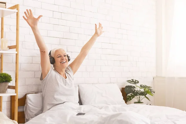 Mujer mayor feliz en auriculares escuchando música en la cama — Foto de Stock