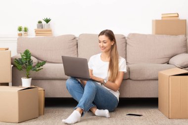 Young smiling woman using laptop in new home