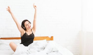 Enerjik kadın yatakta dans ediyor, müzik dinliyor.