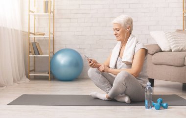 Senior woman in headphones networking on cellphone