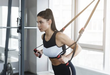 Beautiful young woman using cable machine in sports club