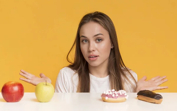 Mujer dudosa eligiendo entre comida sana y malsana, frutas y dulces — Foto de Stock