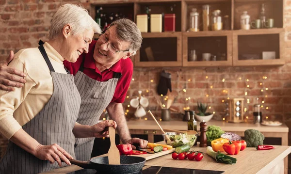 Feliz pareja de ancianos abrazando y uniéndose mientras cocinan la cena juntos —  Fotos de Stock