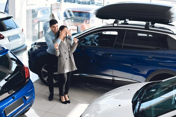 Husband Covering Wifes Eyes Showing New Car In Auto Dealership — Stock Photo, Image