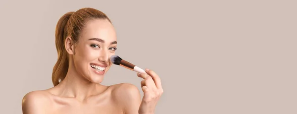 Femme appliquant la poudre de visage faisant le maquillage sur fond beige, Panorama — Photo