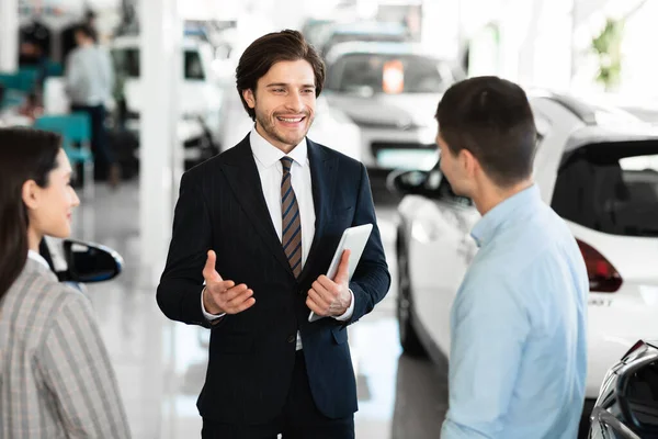 Car dealer talking with clients selling them automobile — Stockfoto