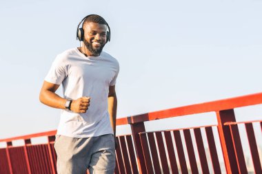Smiling african guy running along the bridge
