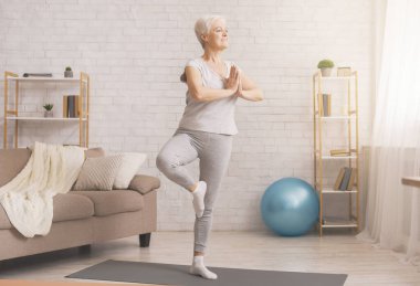 Senior woman doing yoga tree pose at home, free space