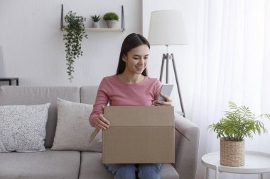 Positive client using cellphone for online shopping while open cardboard box