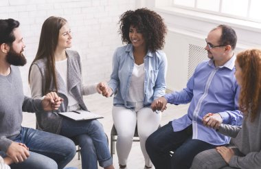 Young multi-cultural group of people holding hands during therapy session