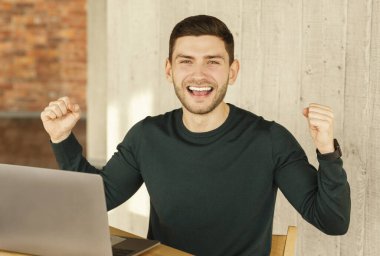Happy Man Shaking Fists Sitting Celebrating Promotion In Modern Office