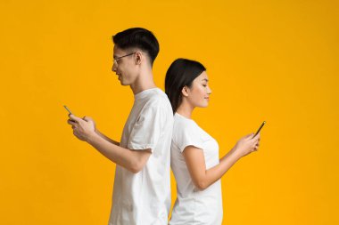 Asian couple standing back to back, using cellphones